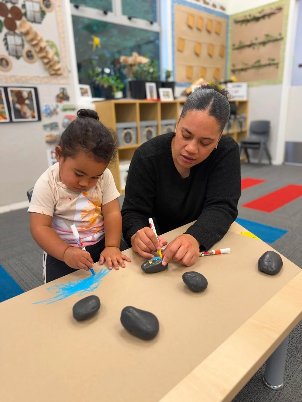 A puapi‘i and tamaiti decorating stones together during Penipeni