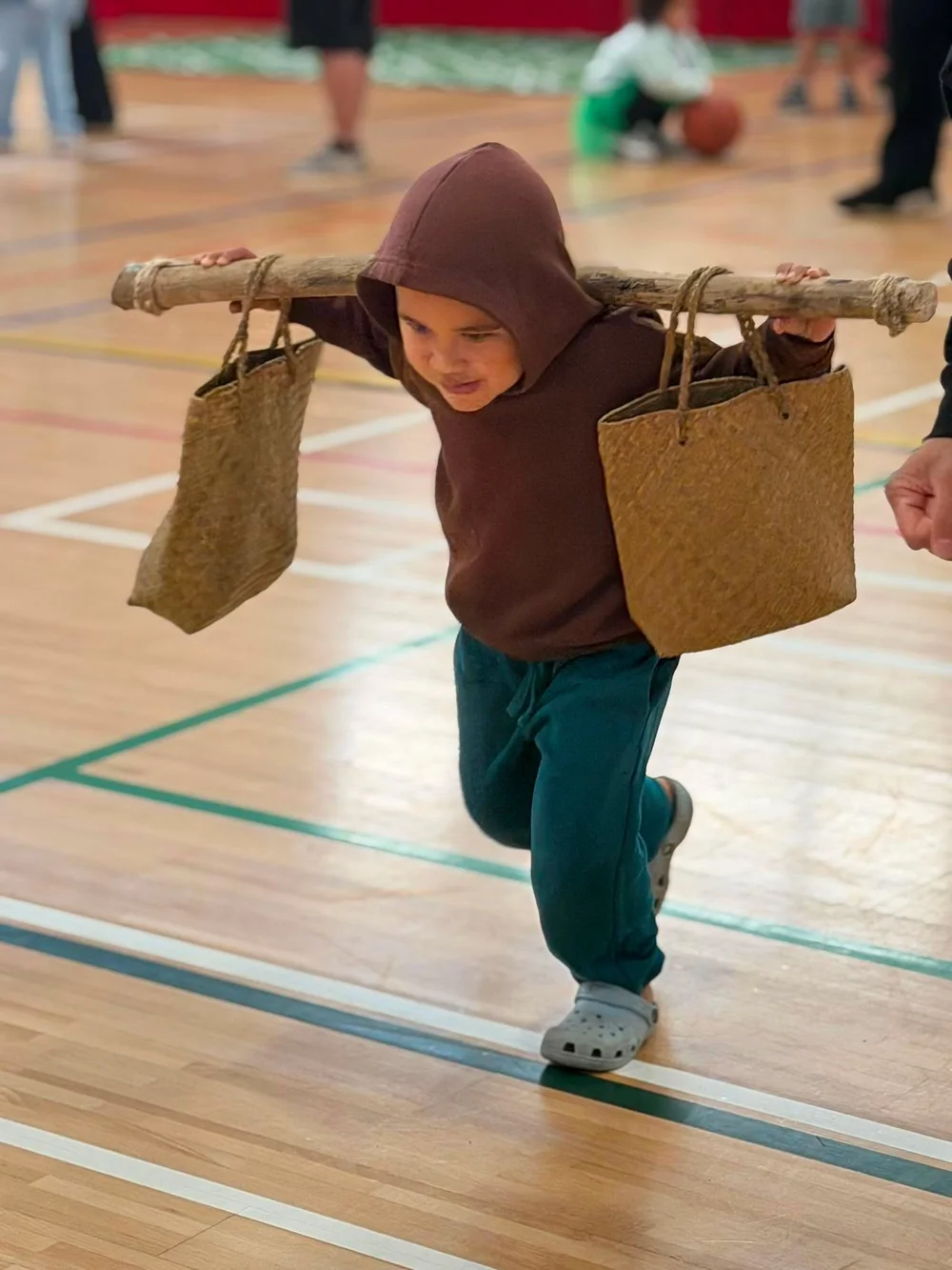 A tamaiti taking part in a cultural game with woven baskets on sports day